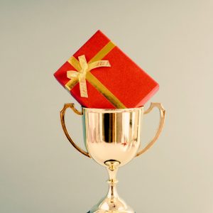 Stock image showing gold trophy with a red and gold gift box in the top